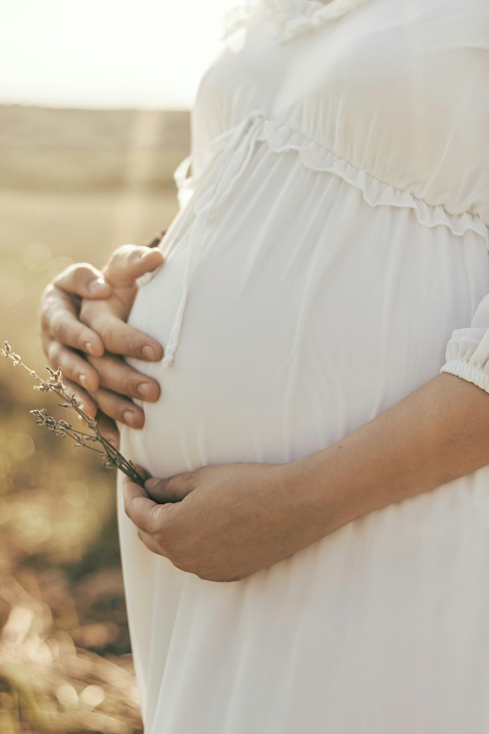 Femme enceinte en robe blanche tenant son ventre dans la nature — coaching maternité et accompagnement périnatal